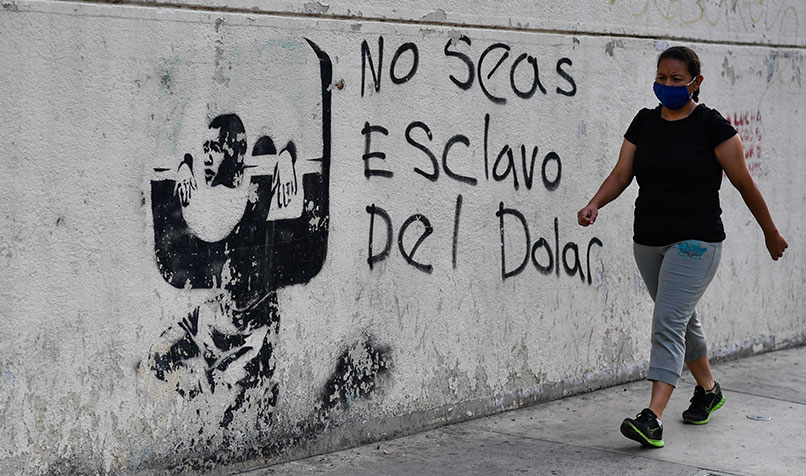 A woman wearing a face mask walks past graffiti, translated as “don’t be a slave of the dollar”, in Caracas, Venezuela.